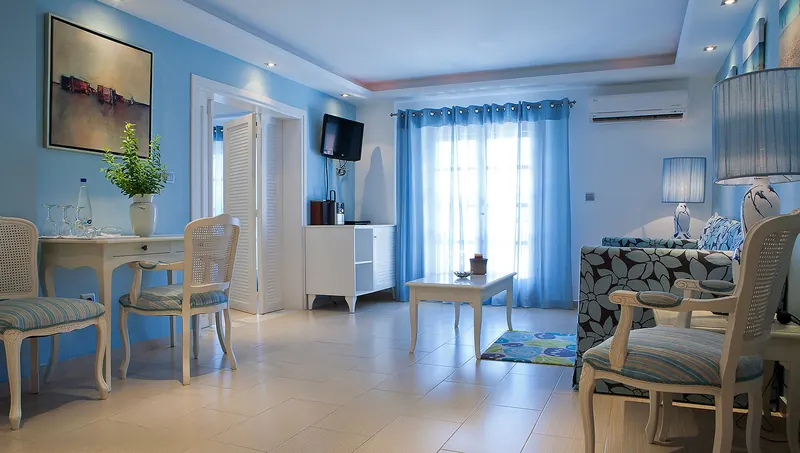 A bright suite with blue walls, cream furniture and doors to the balcony